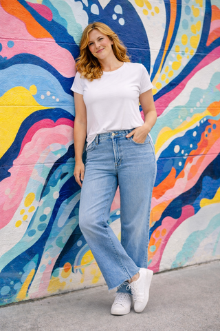 Woman in a white t-shirt and blue jeans standing in front of a colorful mural.