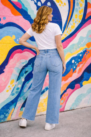 Person wearing a white t-shirt and blue jeans standing in front of a colorful mural.