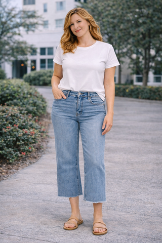 Woman wearing a white t-shirt and blue jeans standing outdoors.