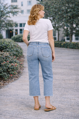 Woman wearing a white t-shirt and light blue jeans walking outdoors.