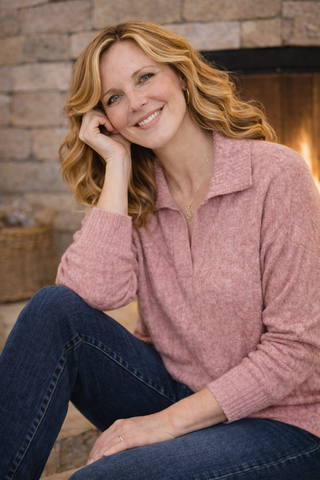 Woman wearing a pink sweater and blue jeans sitting in front of a stone wall.
