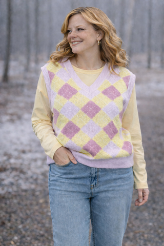 Woman wearing a yellow sweater with a pink and purple argyle pattern in a forest setting
