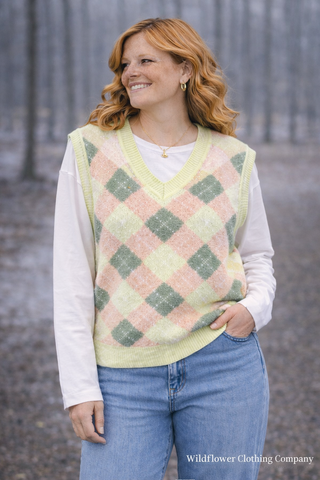Woman wearing a checkered vest over a white shirt with blue jeans, standing outdoors.